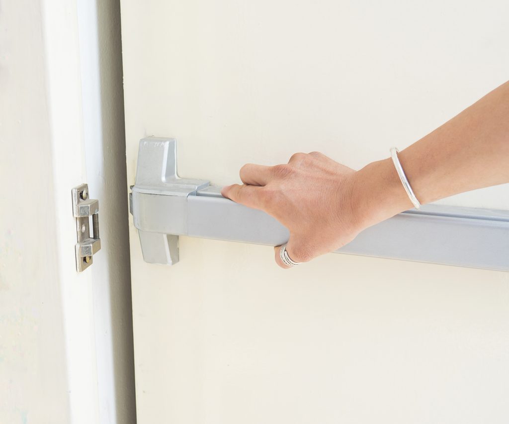 Person operating a fire door push bar during a fire door inspection to check emergency exit functionality and compliance with fire safety regulations.