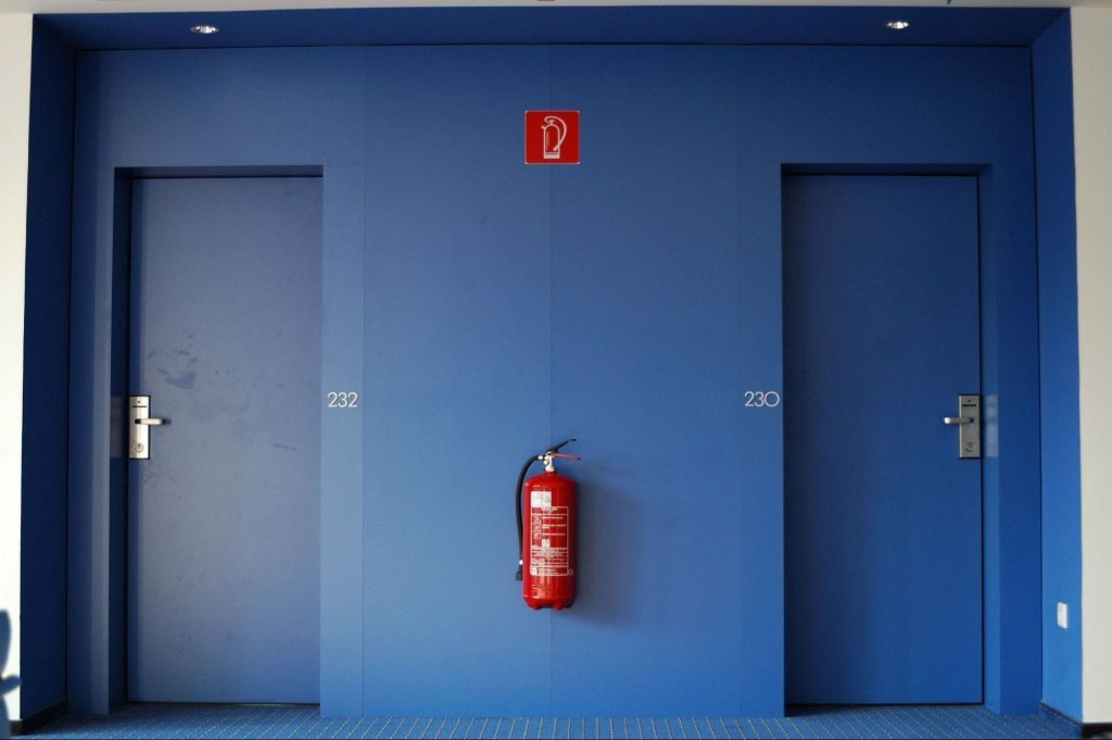Fire extinguisher mounted in a communal building corridor between fire doors, illustrating how often fire extinguishers should be inspected as part of routine fire safety maintenance.